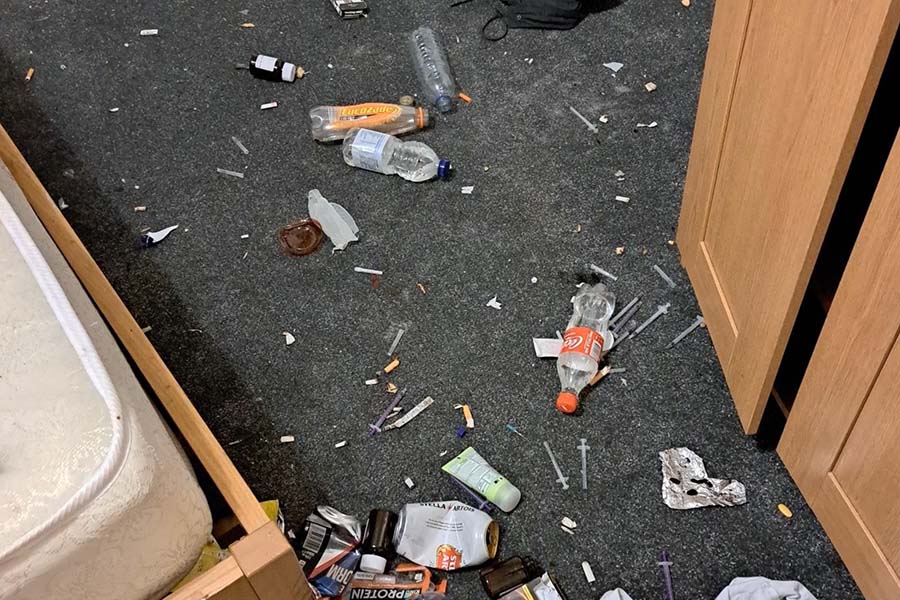 Used hypodermic needles lay on the floor of a bedroom mixed in with other rubbish