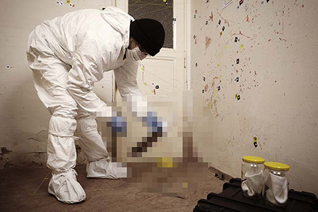 A crime scene cleaner wearing full PPE inspects an item