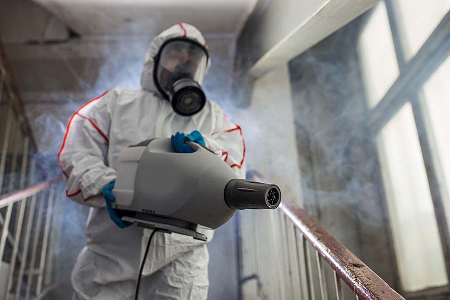 Operator in a protective suit conducts disinfection in contaminated area.