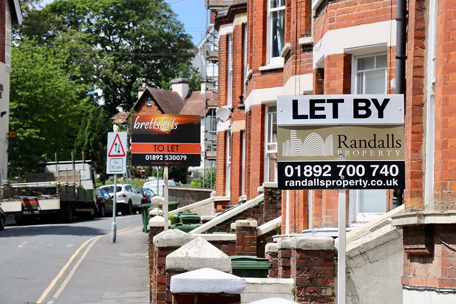 A UK street with a 'Let By' sign outside the property.