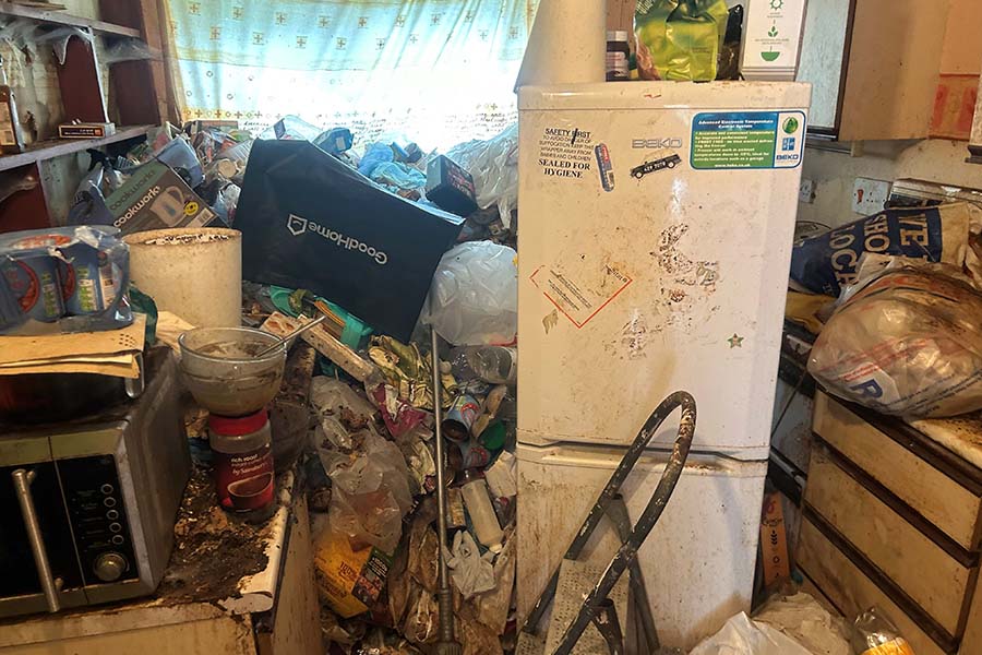 The kitchen at the property of a hoarder filled with rubbish and random items including a fridge, step ladder and others