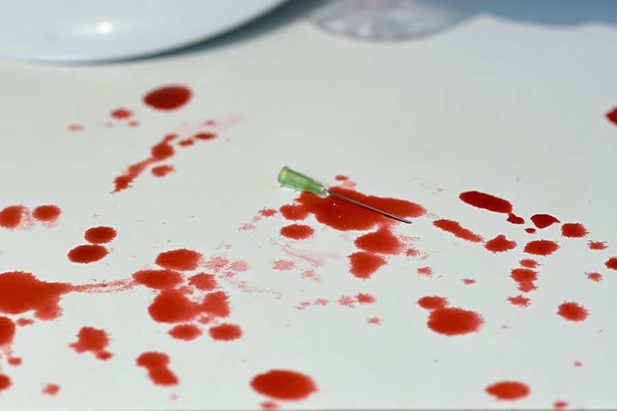 A syringe laying amongst pools of blood on a work surface